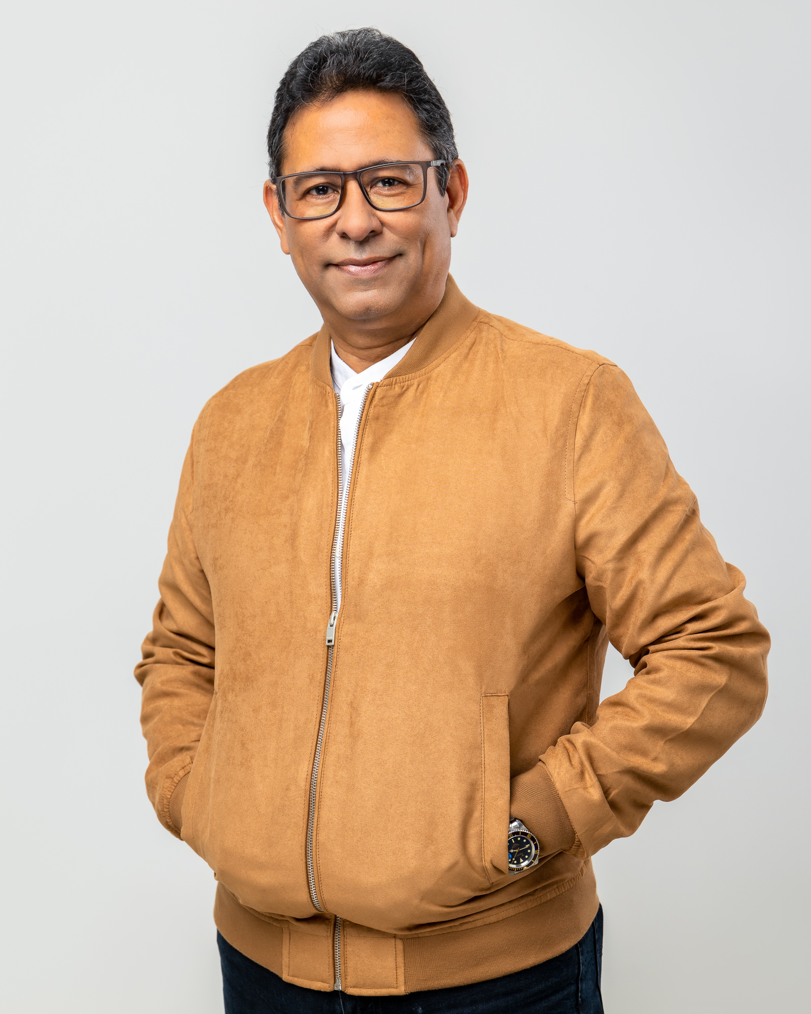 Retrato de medio cuerpo del ejecutivo Orlando Fujitsubo sonriendo con confianza y la mano en la barbilla en actitud analítica. Viste un elegante saco azul marino y un reloj clásico, destacando sobre un fondo negro sólido. La imagen transmite profesionalismo, experiencia corporativa y liderazgo empresarial.