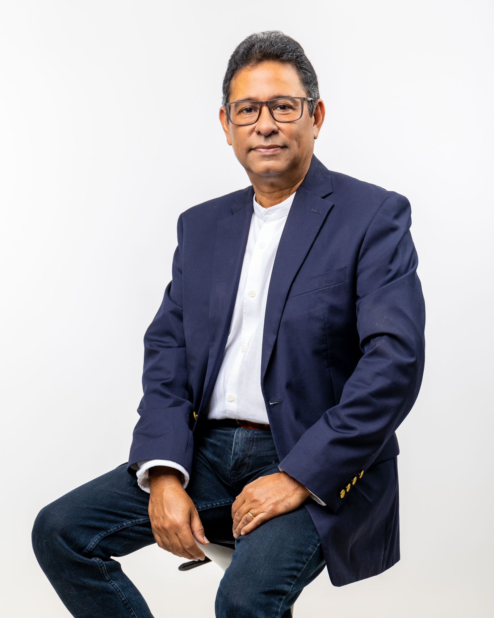 Retrato de medio cuerpo del ejecutivo Orlando Fujitsubo sonriendo con confianza y la mano en la barbilla en actitud analítica. Viste un elegante saco azul marino y un reloj clásico, destacando sobre un fondo negro sólido. La imagen transmite profesionalismo, experiencia corporativa y liderazgo empresarial.